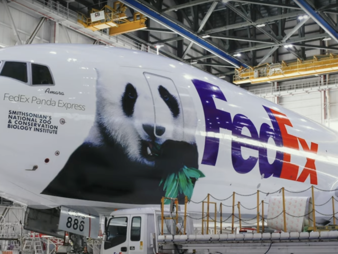 Photo of a large plane in an airplane hangar with the FedEx logo and an image of a giant panda on the side along with the words, "FedEx Panda Express"